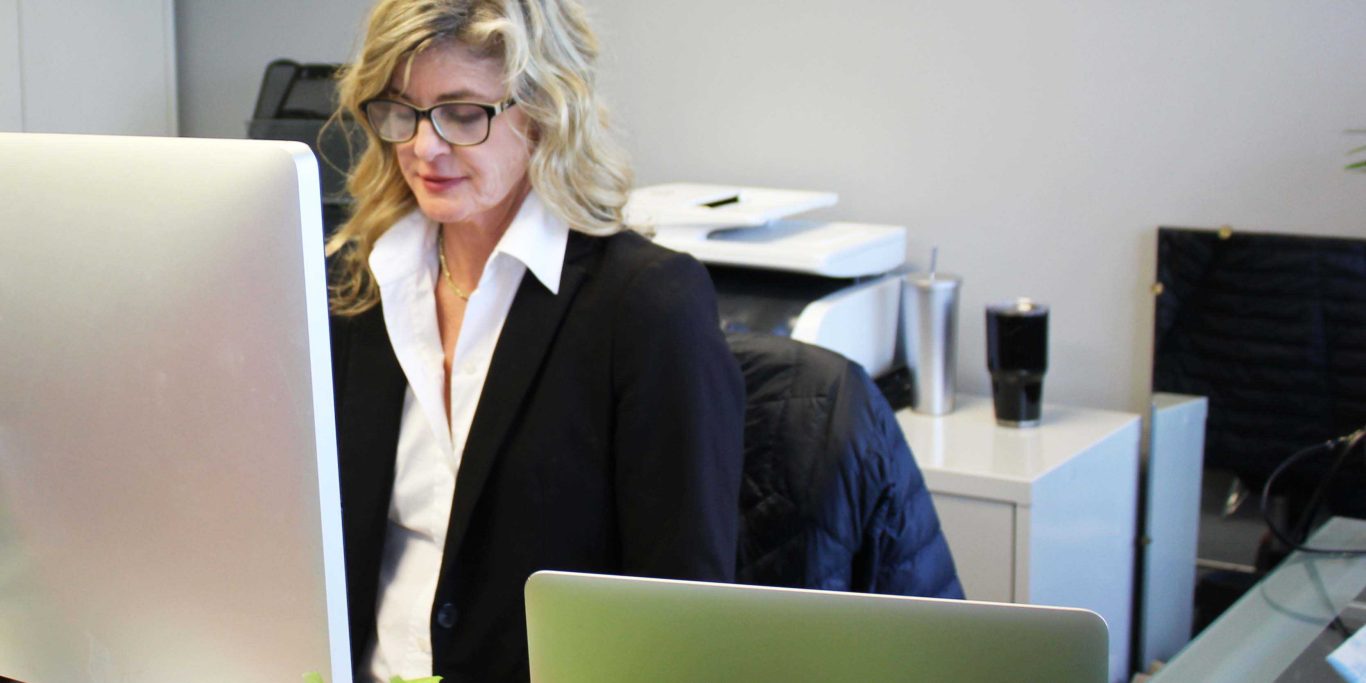 Blonde woman in a black suit wearing glasses working behind a Mac Desktop at Tamburrino, INC in Memphis, TN